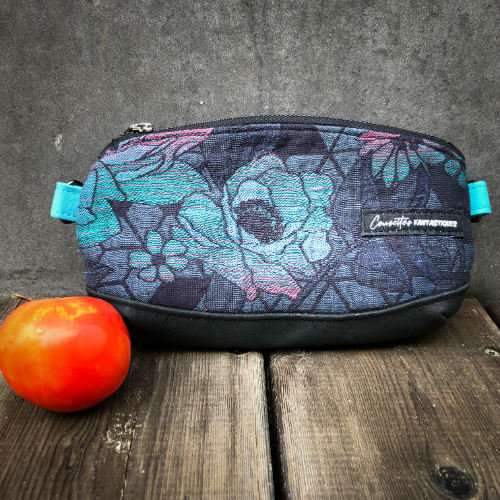 A small zippered clutch sewn in black cork and a babywearing wrap with geometric and floral patterns in shades of blue, green, and pink.