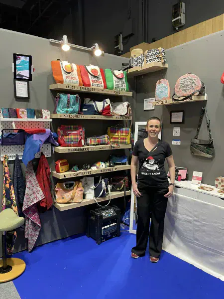 Marie Alhomme devant son stand au Salon du Made in France 2024 — créations en maroquinerie et accessoires exposées sur des étagères en bois.