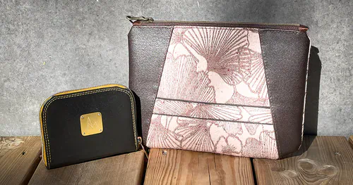 Pochette Pyramide N-07 et Mini Portefeuille En Ville Millésime 2022 en peau de marc de raisin Nisiar, posés sur une terrasse en bois.