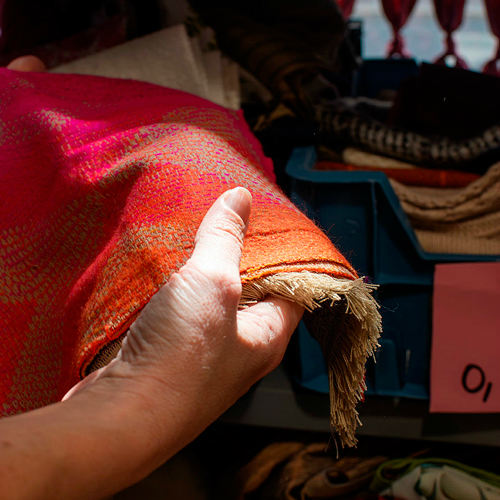 Une main blanche manipule un tissu dans les tons orangés parmi d'autres
