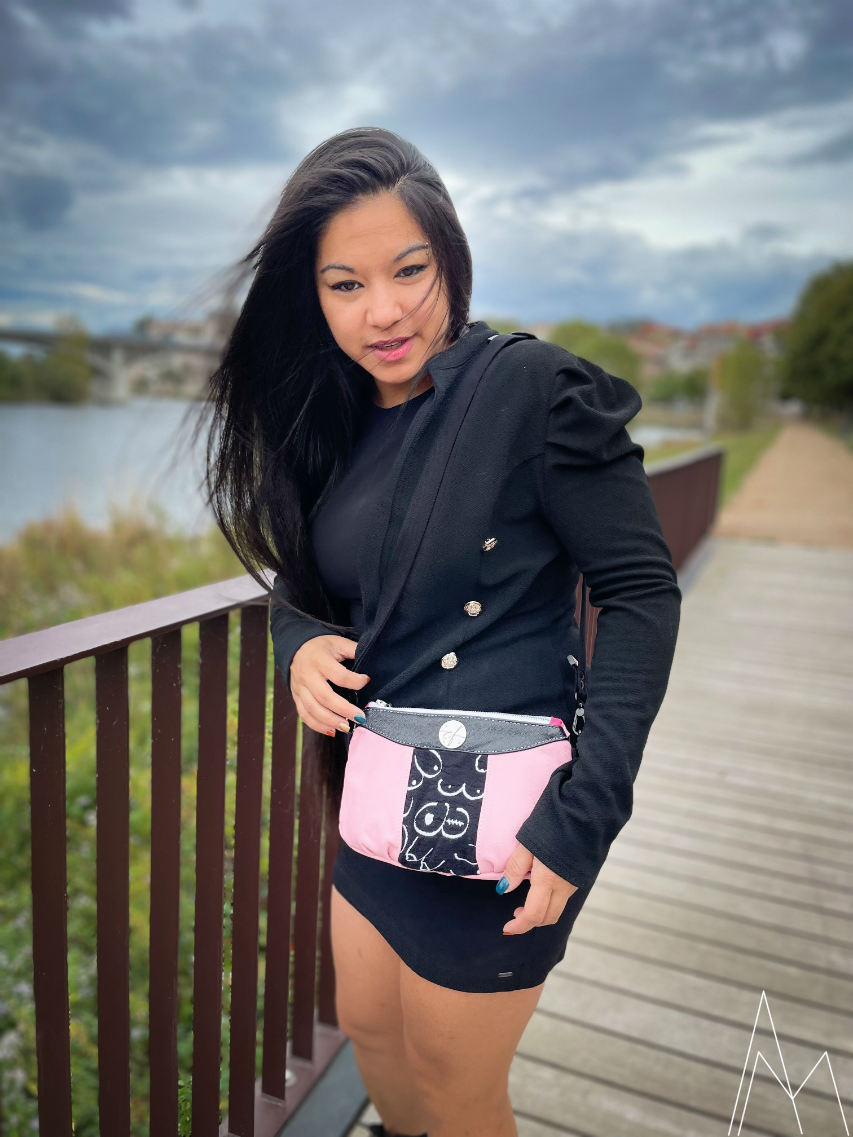 Photo of a young woman with a tan complexion carrying a pink and black clutch, in an outdoor park during the day.