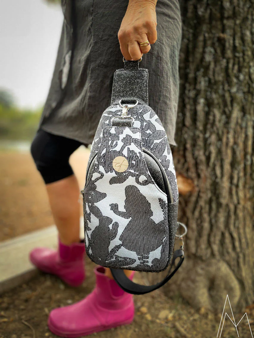 Photo d'une femme mûre portant à la main un sac à dos gris et bleu, dans un parc en extérieur, de jour.