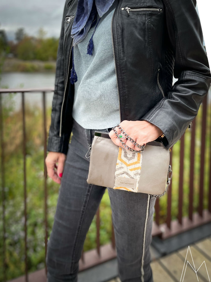 Photo of a mature white woman carrying a gray and yellow clutch, in an outdoor park during the day.