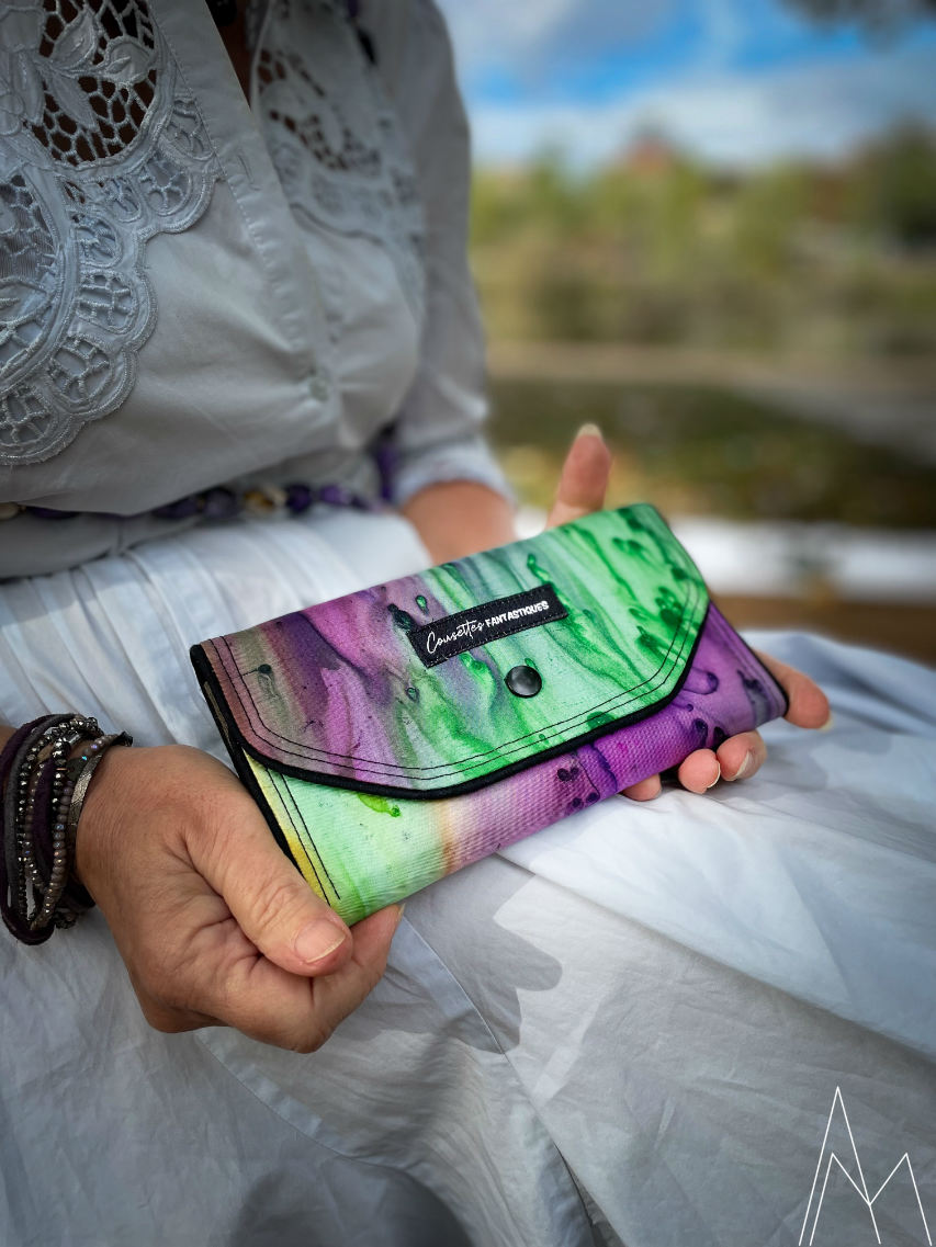 Photo of a mature white woman holding a wallet in shades of green and purple, in an outdoor park during the day.