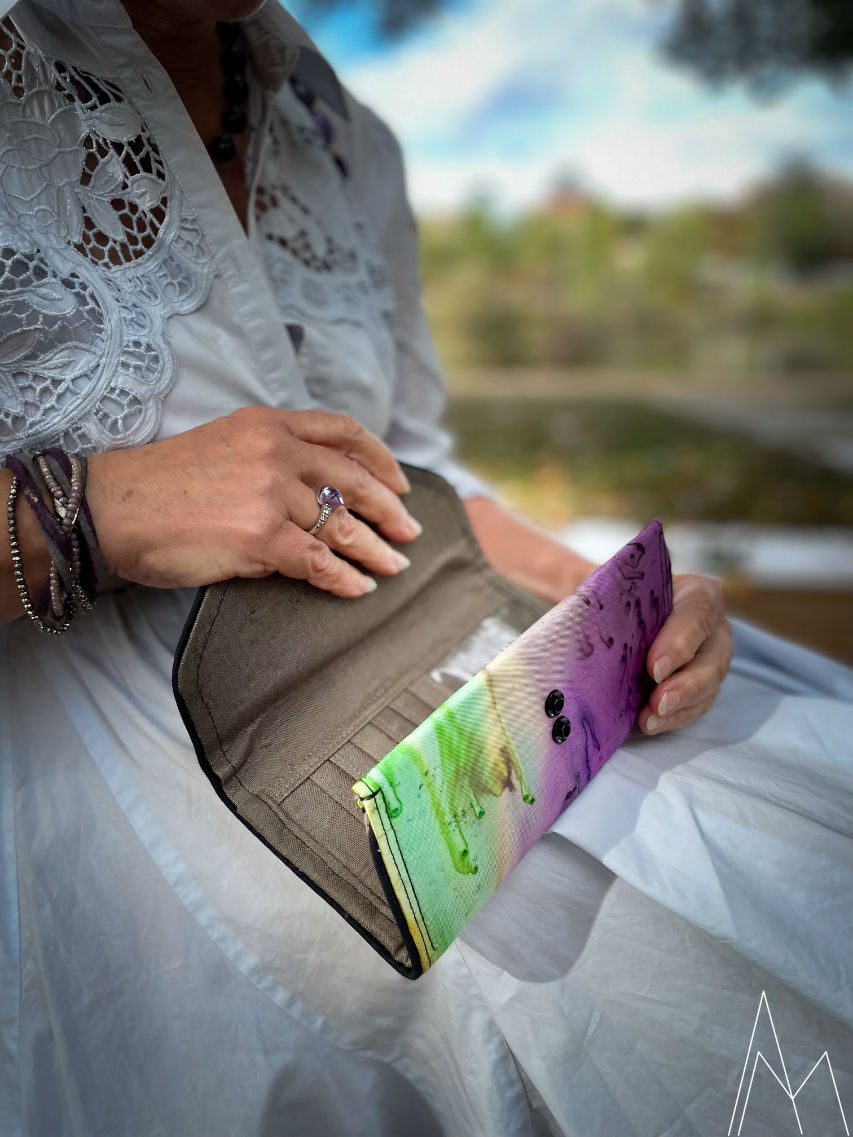 Photo of a mature white woman carrying a wallet in shades of green and purple, in an outdoor park during the day.
