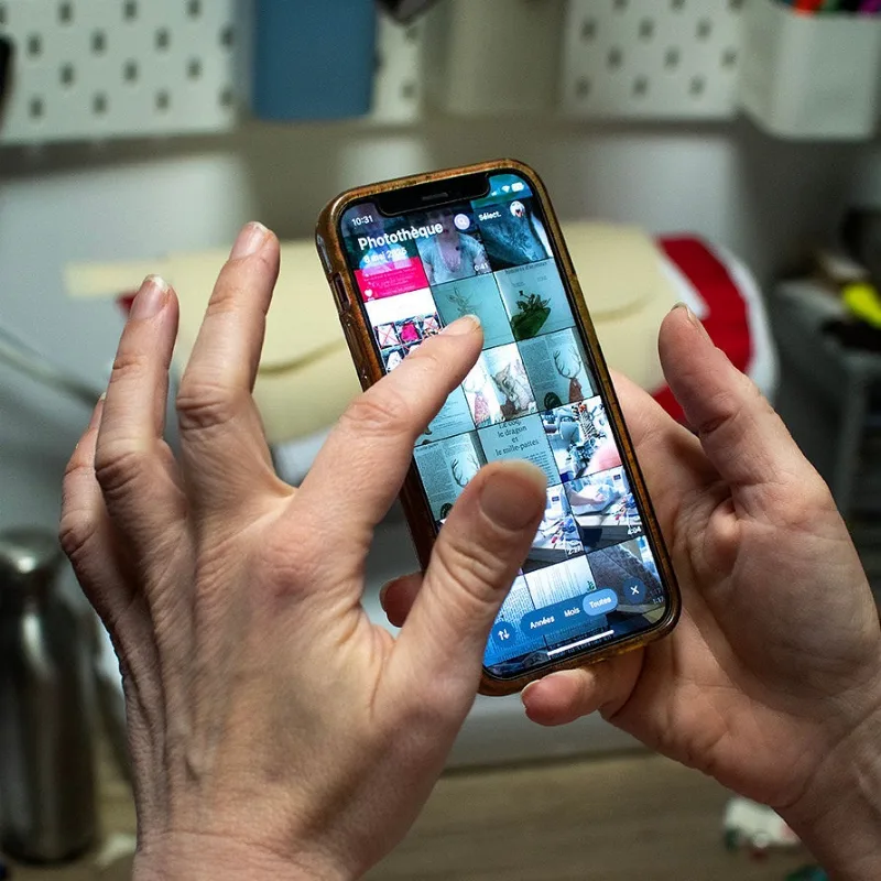 Les mains de Marie font défiler des photos sur son téléphone, à l’atelier