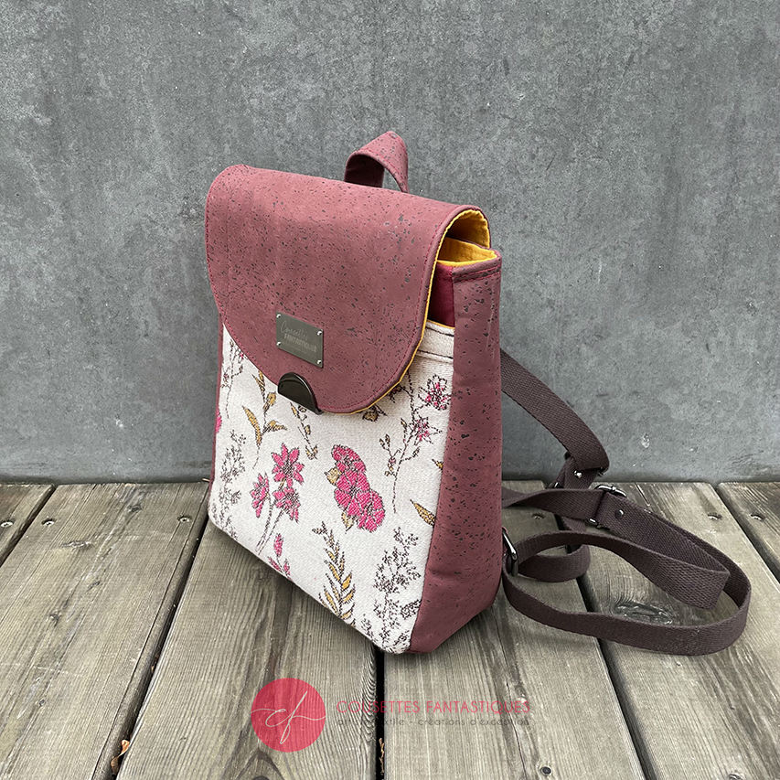 A backpack made with scarf fabric in floral patterns in pink tones on ecru background and brick cork.