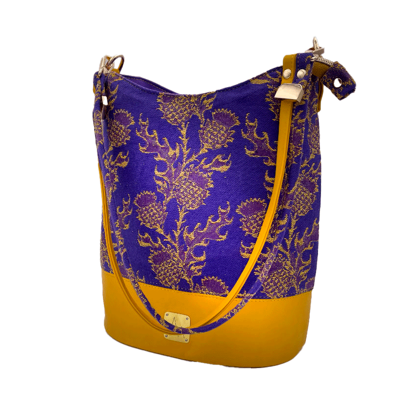 A bucket bag made from babywearing wrap fabric featuring yellow thistles on a purple background with yellow lamb leather.