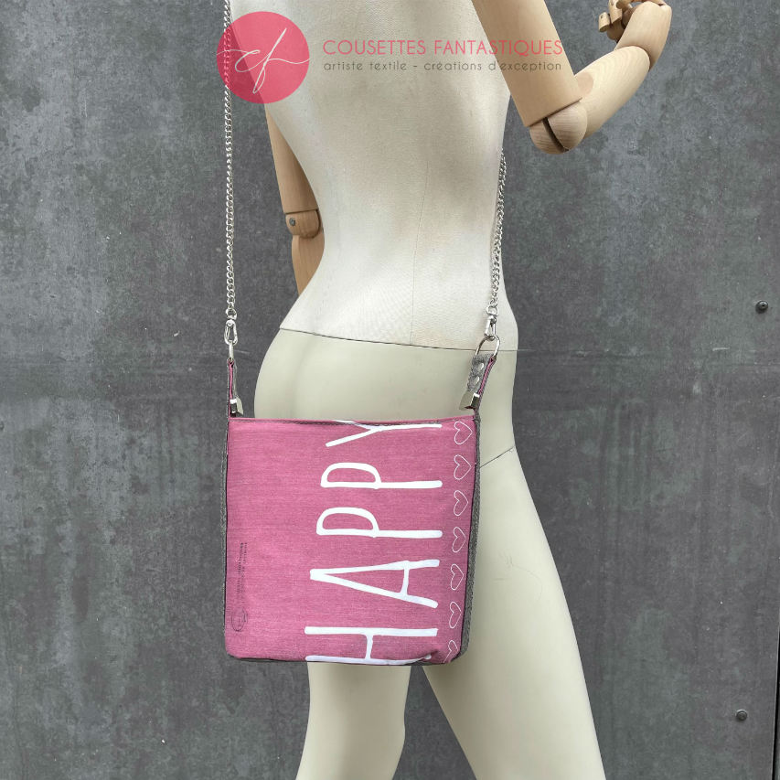 A small “bucket” bag made with delicate pink canvas featuring the word “Happy” and gray ostrich-patterned faux leather.