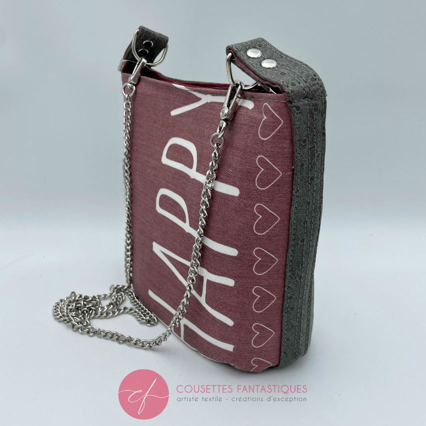 A small “bucket” bag made with delicate pink canvas featuring the word “Happy” and gray ostrich-patterned faux leather.