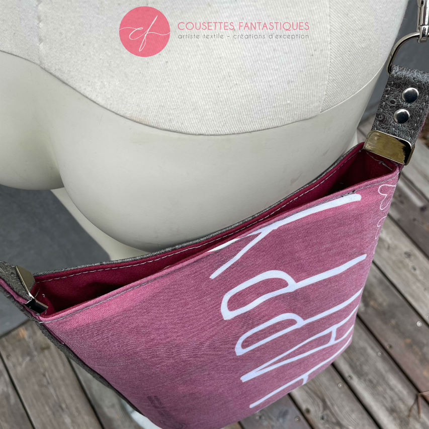 A small “bucket” bag made with delicate pink canvas featuring the word “Happy” and gray ostrich-patterned faux leather.