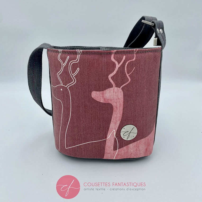 A small “bucket” bag made with delicate pink canvas featuring two white deer silhouettes and gray high-fashion denim.