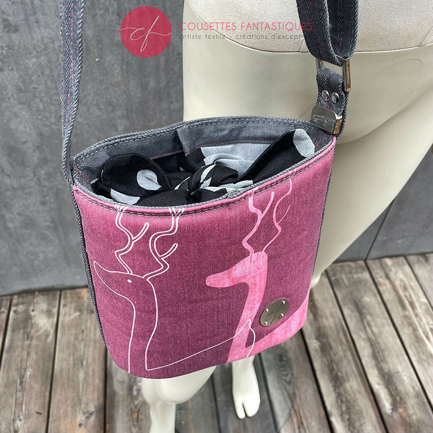 A small “bucket” bag made with delicate pink canvas featuring two white deer silhouettes and gray high-fashion denim.