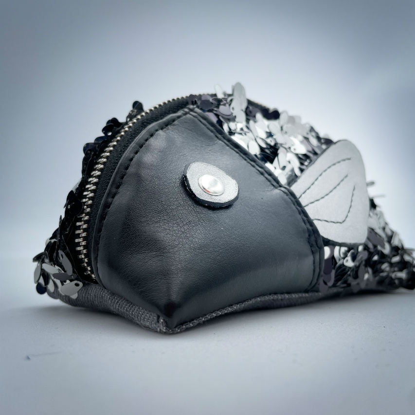 A zippered pouch sewn with black faux leather, black and white sequined fabric, and gray denim.