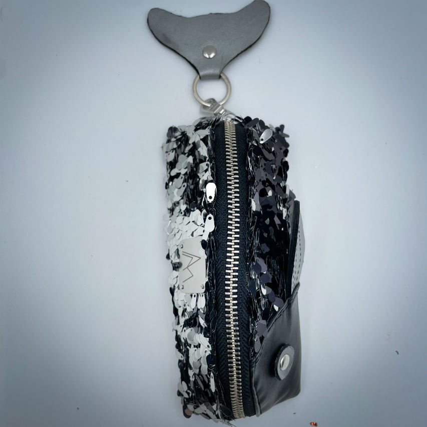 A zippered pouch sewn with black faux leather, black and white sequined fabric, and gray denim.