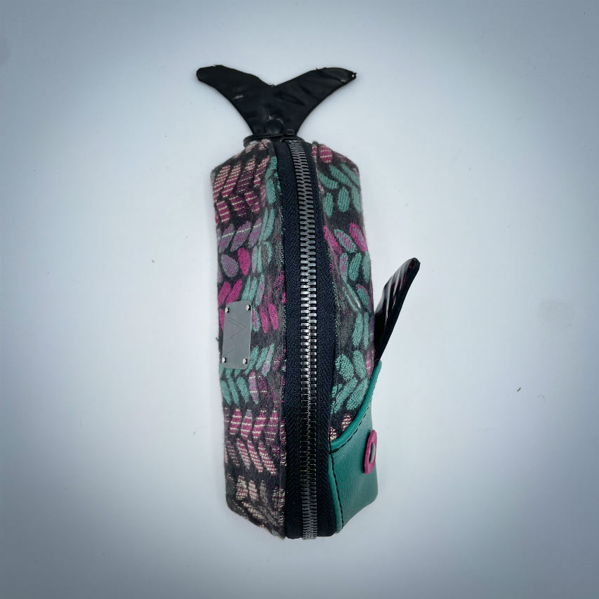 A zippered pouch sewn from sage green leather, black patent leather, fuchsia pink leather, and two scraps of a babywearing wrap with a green, beige, and pink mesh pattern on a black background.