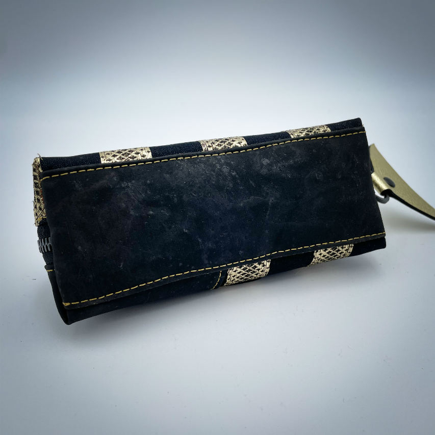 A zippered pouch sewn with black cork, black voile with golden stripes, and golden metallic leather.