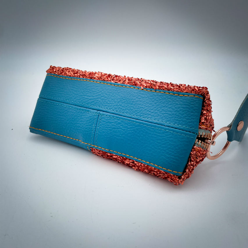 A zippered pouch made from stretch fabric with copper metallic bouclé, turquoise blue faux leather, and bright light mint lining.