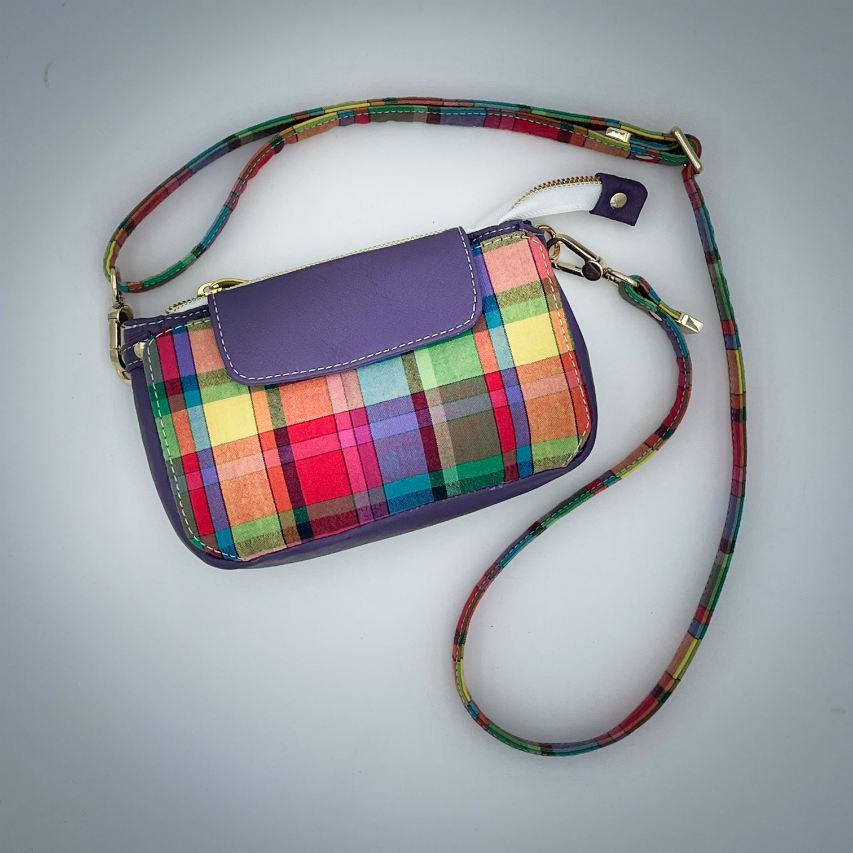 A hybrid clutch wallet bag made of purple leather and multicolored madras fabric.