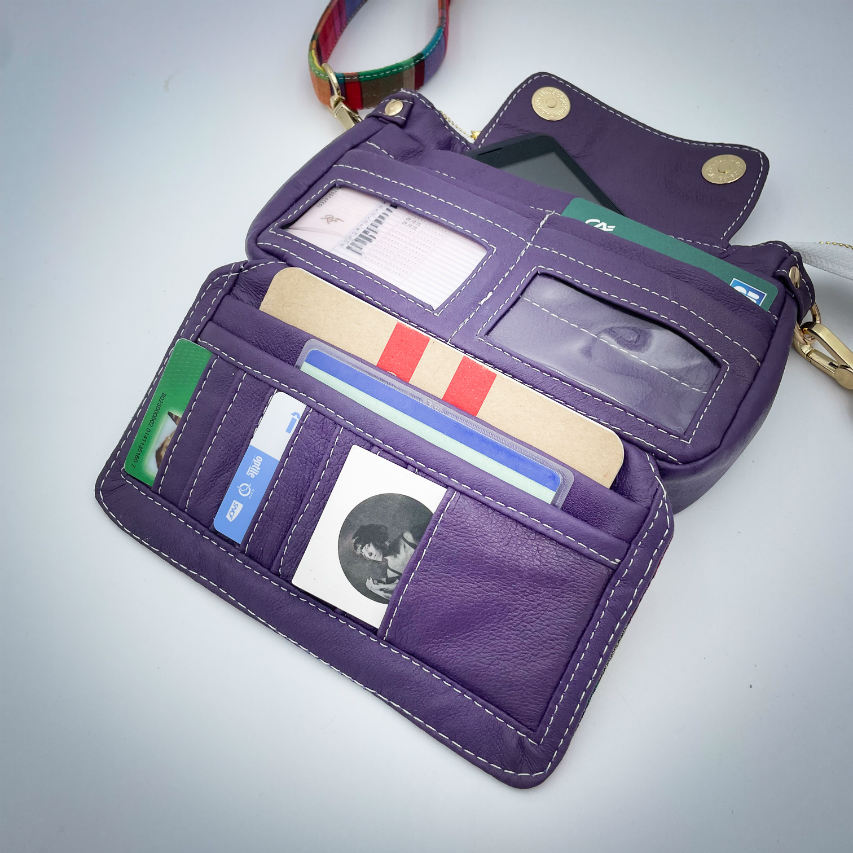 A hybrid clutch wallet bag made of purple leather and multicolored madras fabric.