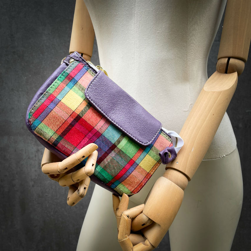 A hybrid clutch wallet bag made of purple leather and multicolored madras fabric.