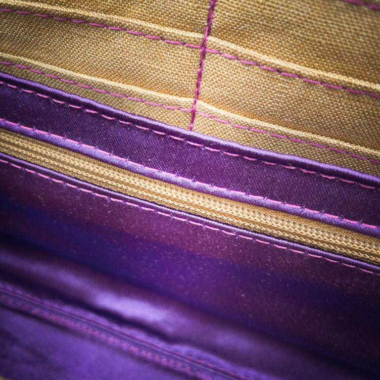 A wallet made from purple and yellow geometrical patterned wrap scrap combined with purple and gold reclaimed faux leathers on the outside, and mustard flax light canvas and deep violet satin on the inside.