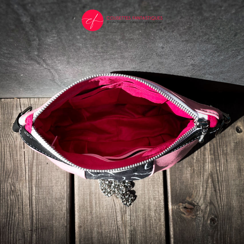 A messenger bag made from a black and white babywearing wrap with stylized breast drawings, black stingray leather, and pink stingray leather.