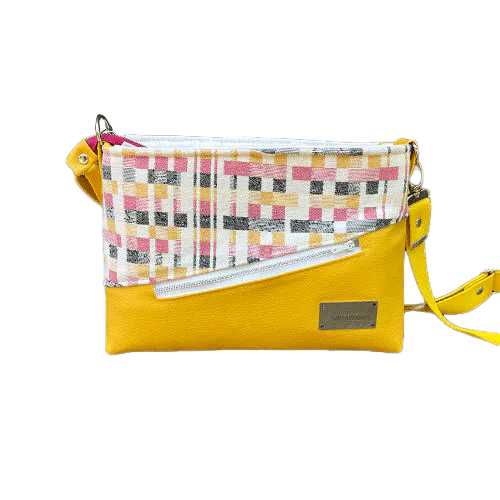 A rectangular messenger bag made from black, white, pink, and yellow babywearing wrap fabric with a geometric pattern, and sunflower yellow faux leather.