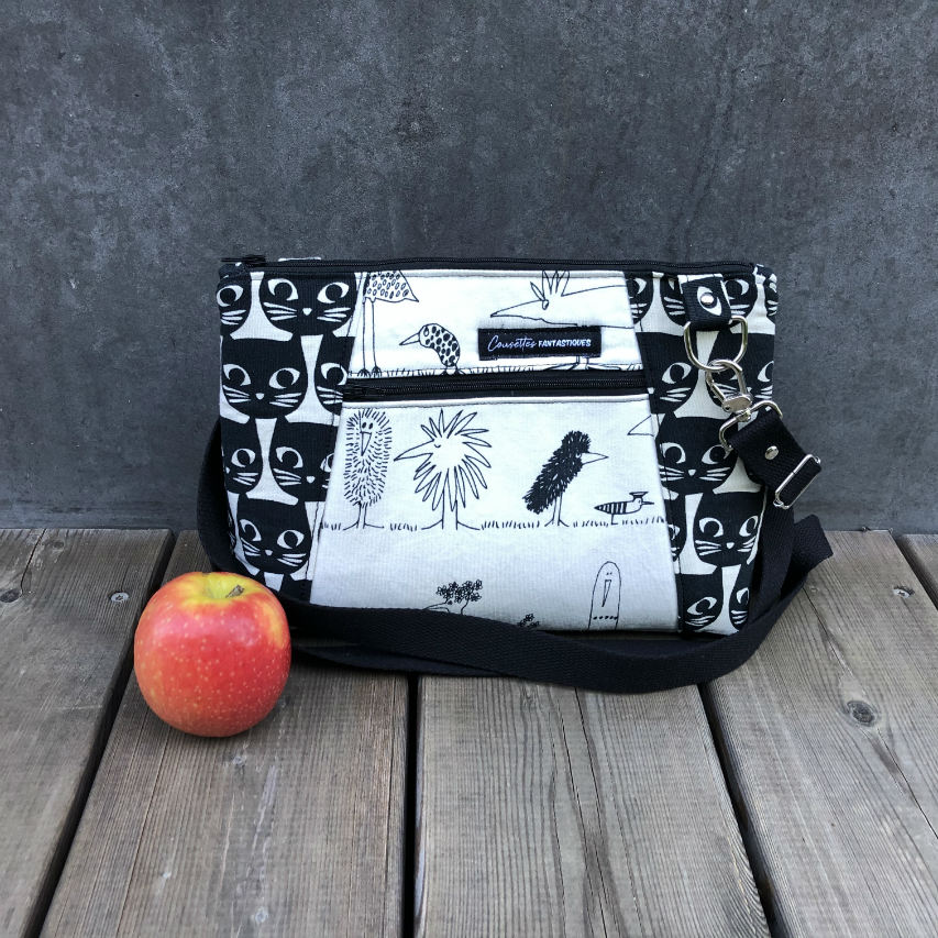 A trapezoid messenger bag made from black and white cotton fabrics on the outside with stylized cat and bird motifs, matched with bird-themed cotton cretonne on the inside.