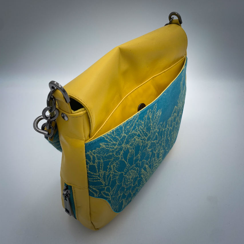 A messenger bag crafted from baby wrap fabric featuring yellow succulents on a turquoise background and sunshine-yellow leather, paired with ice-blue and yellow cotton linings inside.