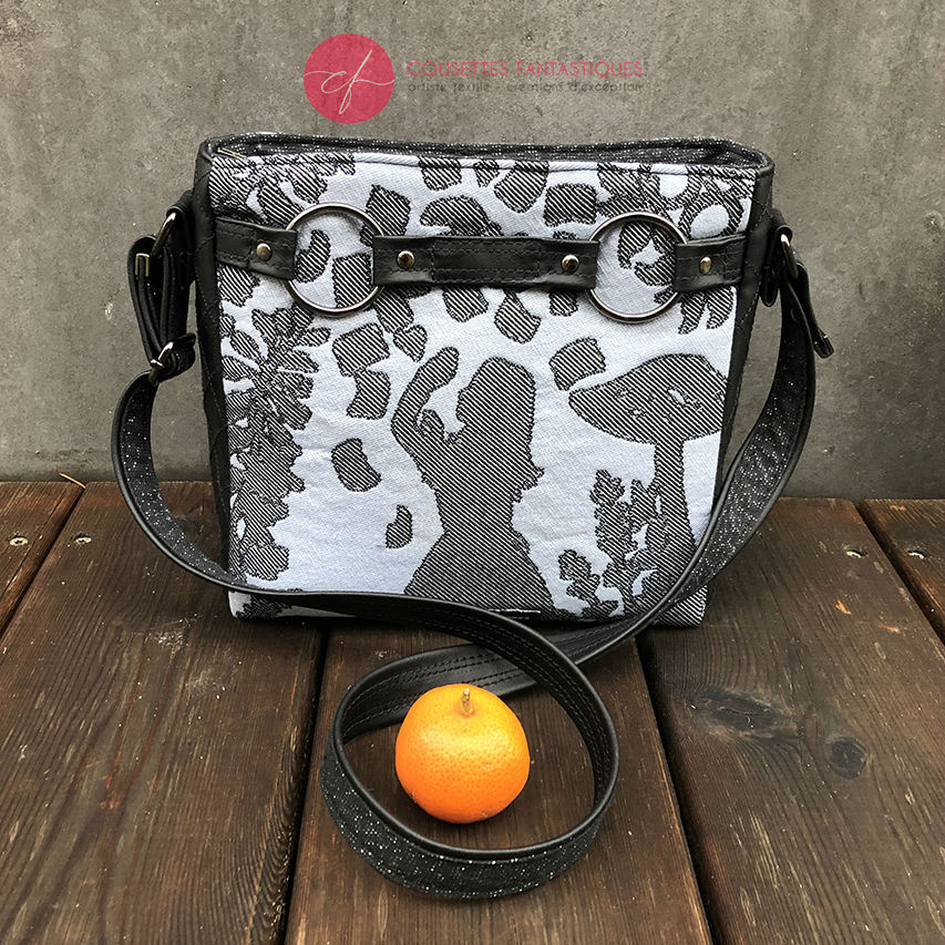 A trapezoid crossbody bag made from a black, gray-blue, and silver “Alice in Wonderland” babywearing scarf, paired with hand-quilted black faux leather.