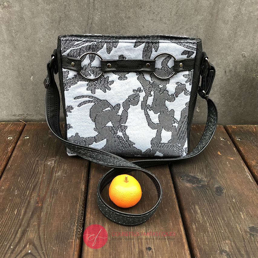 A trapezoid crossbody bag made from a black, gray-blue, and silver “Alice in Wonderland” babywearing scarf, paired with hand-quilted black faux leather.