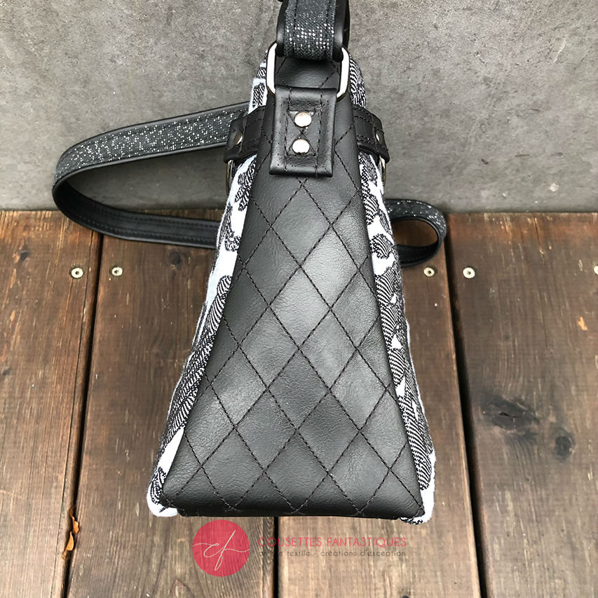 A trapezoid crossbody bag made from a black, gray-blue, and silver “Alice in Wonderland” babywearing scarf, paired with hand-quilted black faux leather.