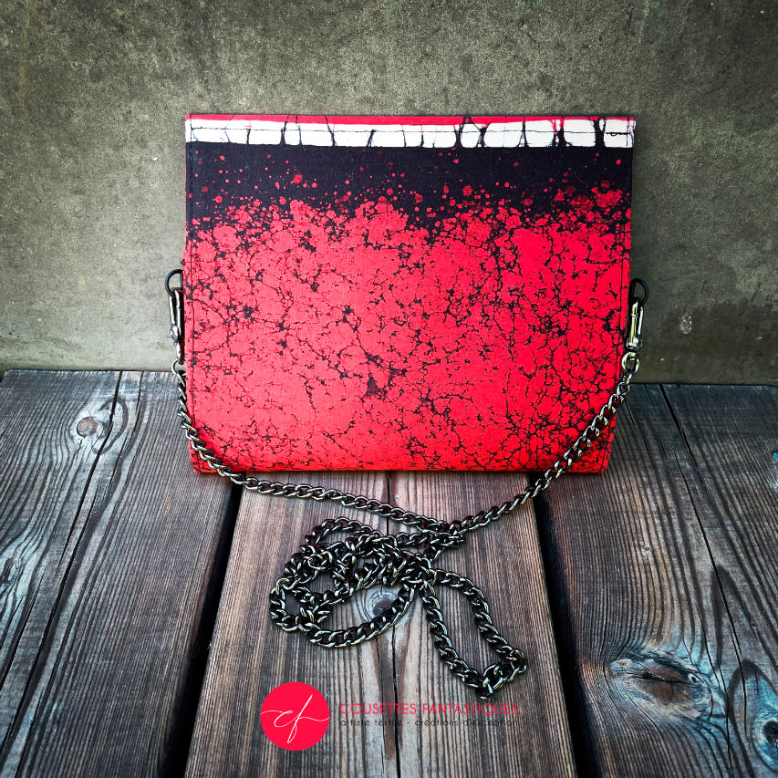 A flat handbag with a flap made of black, white, and red batik cotton fabric.