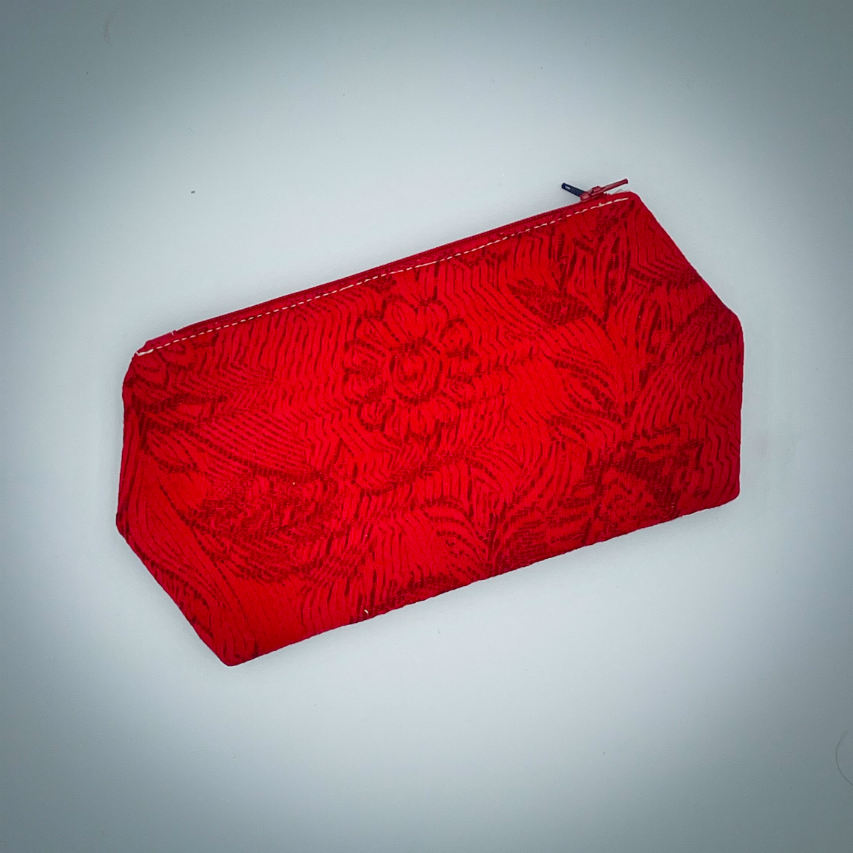 A double zippered pouch sewn from several babywearing wrap scraps (blue and red) and white faux leather.