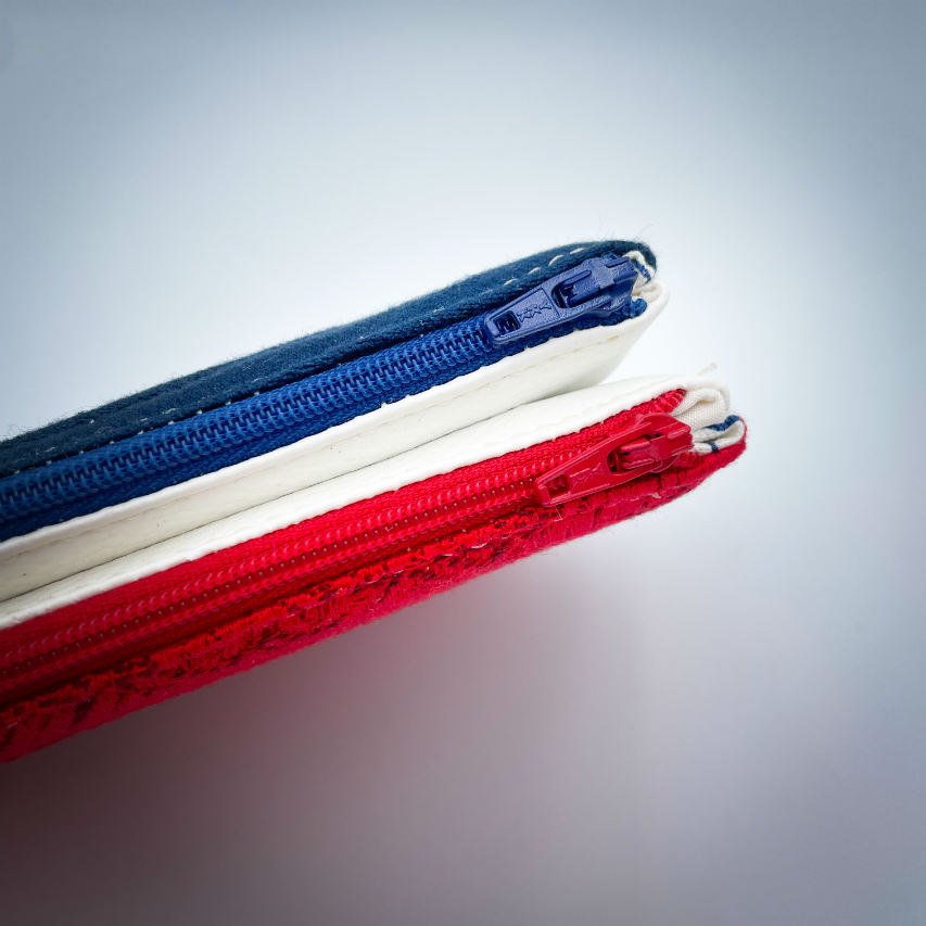 A double zippered pouch sewn from several babywearing wrap scraps (blue and red) and white faux leather.