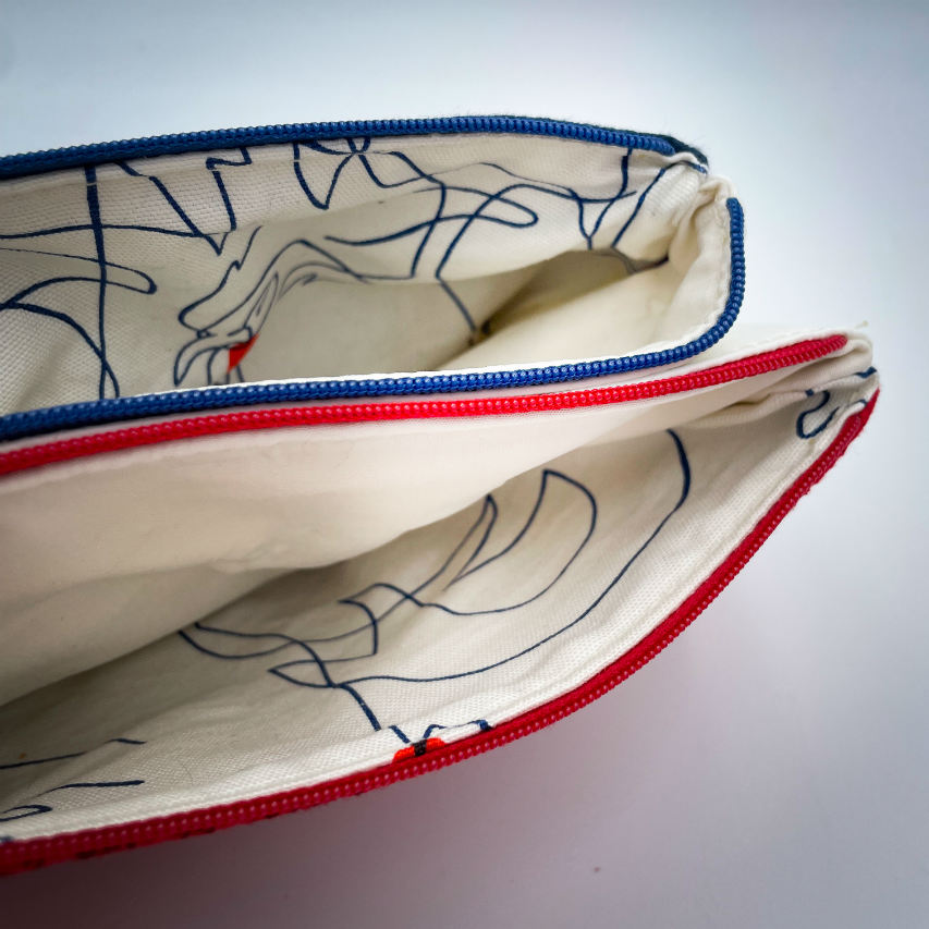 A double zippered pouch sewn from several babywearing wrap scraps (blue and red) and white faux leather.