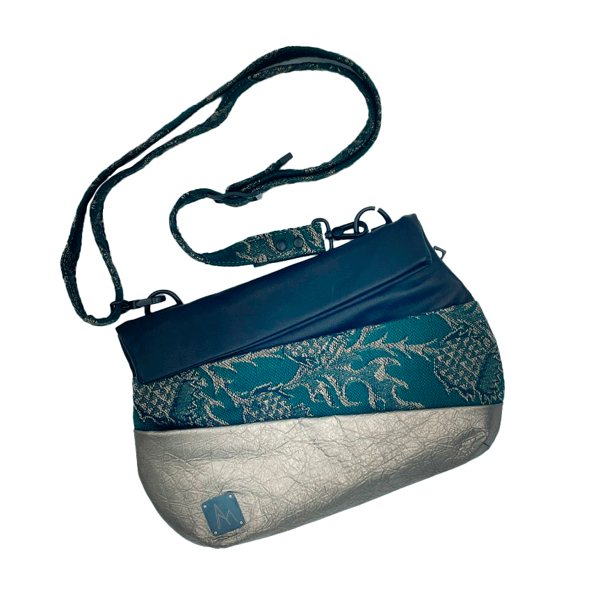 A shoulder bag made from two leathers, gold and black, and a piece of baby wrap fabric in black, green, and gold with a thistle pattern on the outside, and forest green poplin and gold satin on the inside.