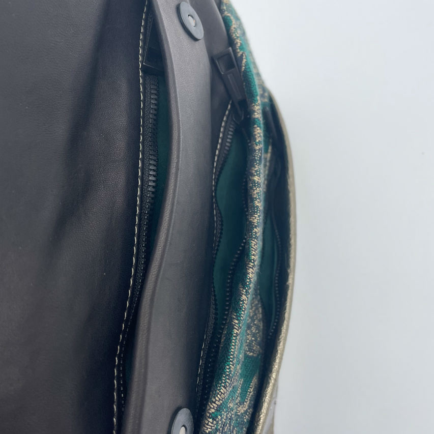 A shoulder bag made from two leathers, gold and black, and a piece of baby wrap fabric in black, green, and gold with a thistle pattern on the outside, and forest green poplin and gold satin on the inside.