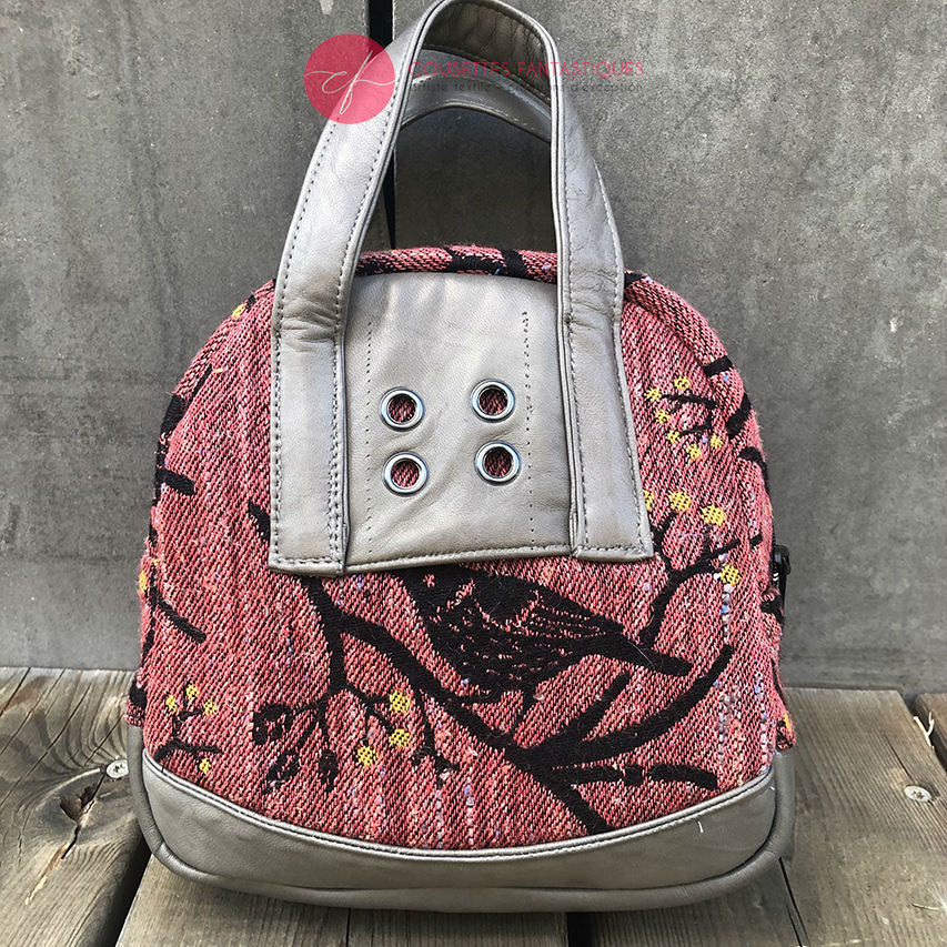 A mini handbag made of babywearing wrap scraps showing birds in a tree in pink and black tones, and grey lambskin leather.