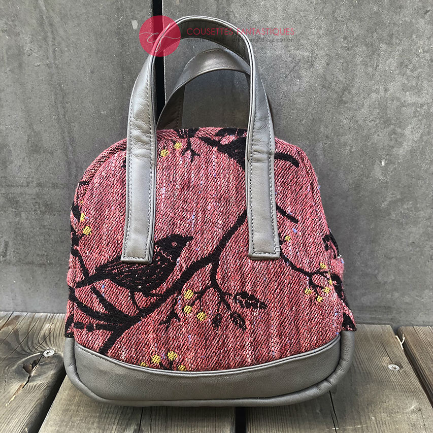 A mini handbag made of babywearing wrap scraps showing birds in a tree in pink and black tones, and grey lambskin leather.