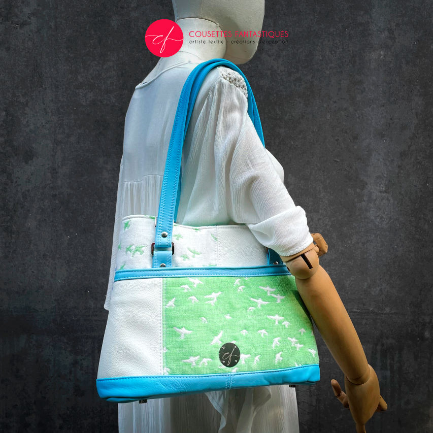 A handbag made of light blue leather and white, light blue, and apple green fabric with a bird motif.