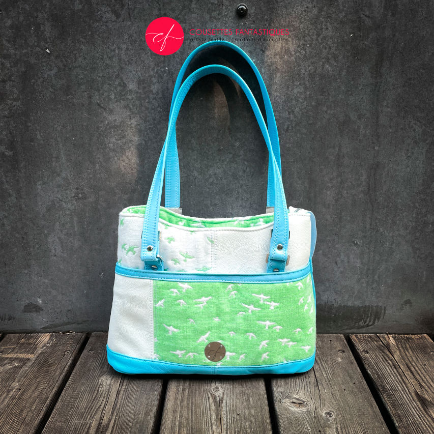 A handbag made of light blue leather and white, light blue, and apple green fabric with a bird motif.