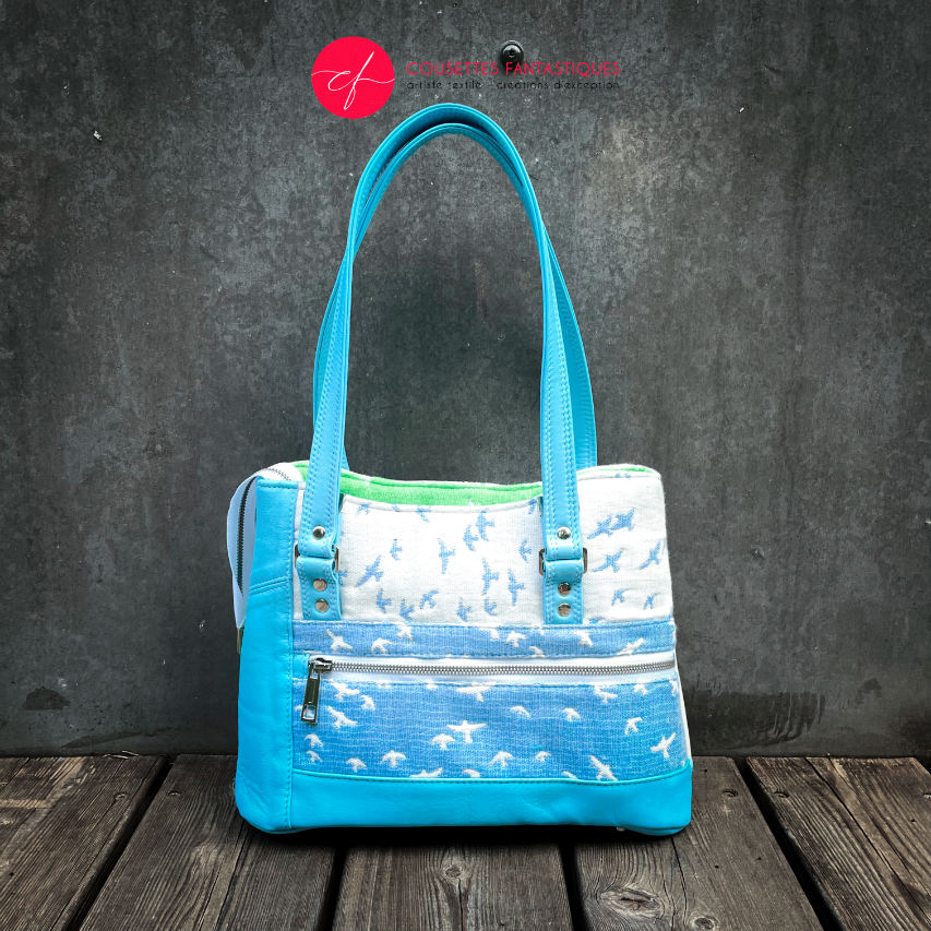 A handbag made of light blue leather and white, light blue, and apple green fabric with a bird motif.