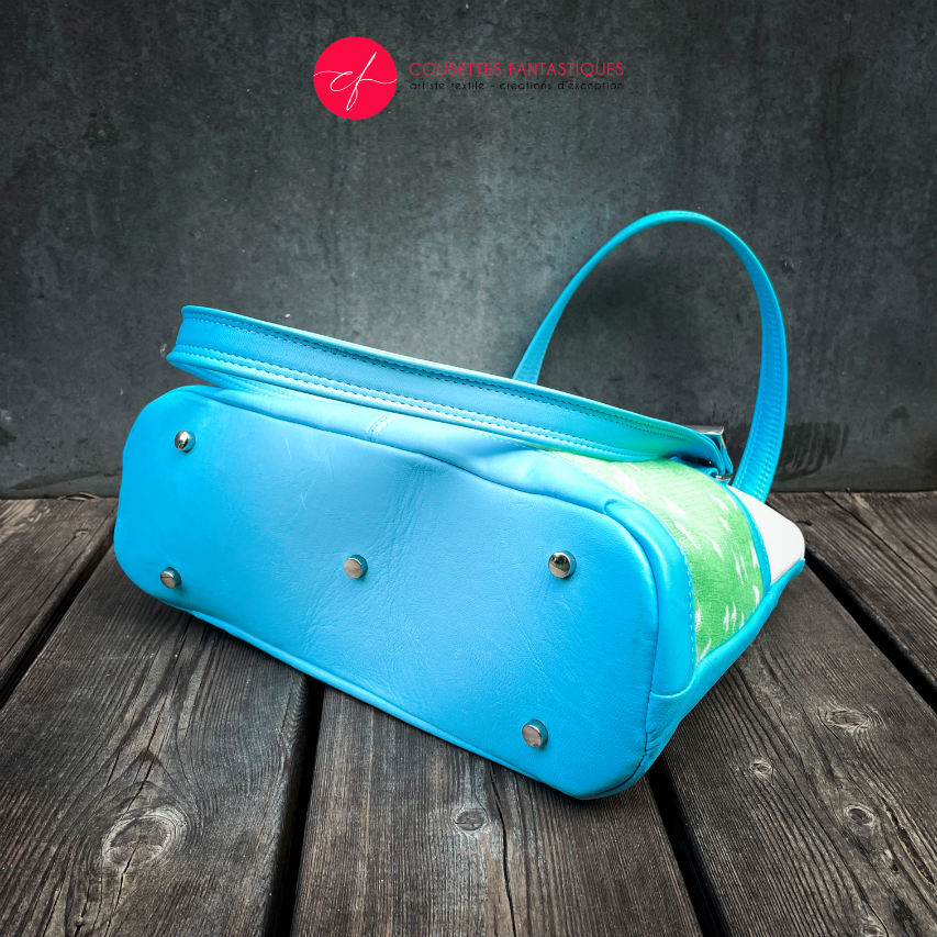 A handbag made of light blue leather and white, light blue, and apple green fabric with a bird motif.