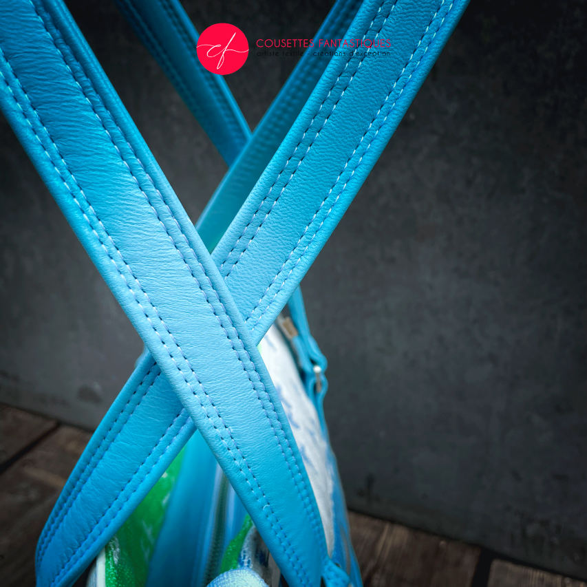 A handbag made of light blue leather and white, light blue, and apple green fabric with a bird motif.