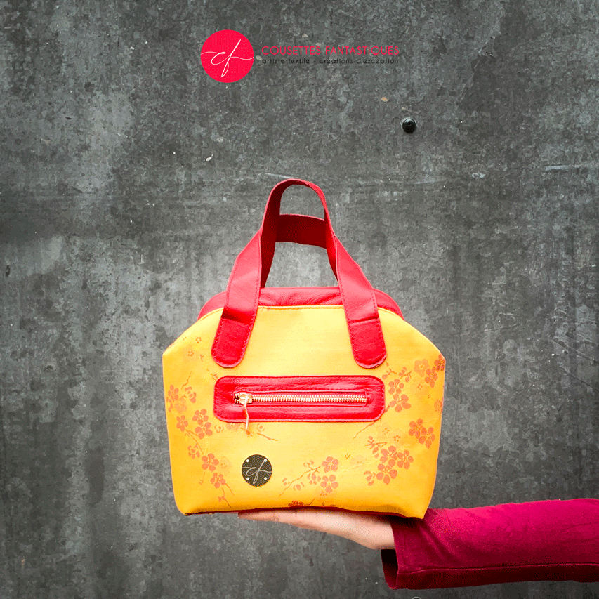 A mini handbag made of yellow upholstery fabric with a red cherry blossom pattern and red leather.