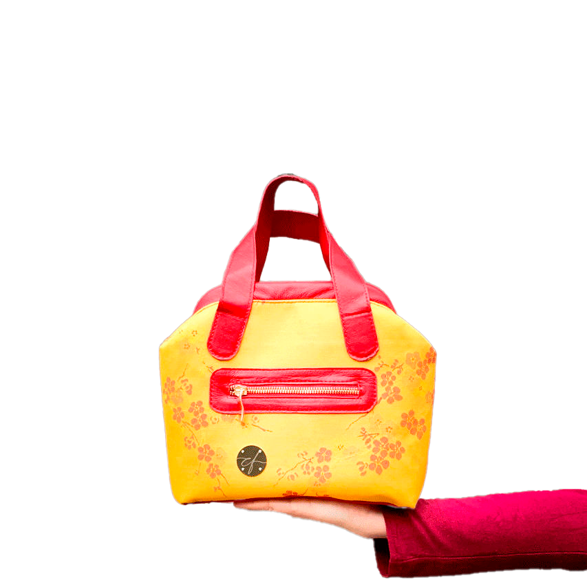 A mini handbag made of yellow upholstery fabric with a red cherry blossom pattern and red leather.