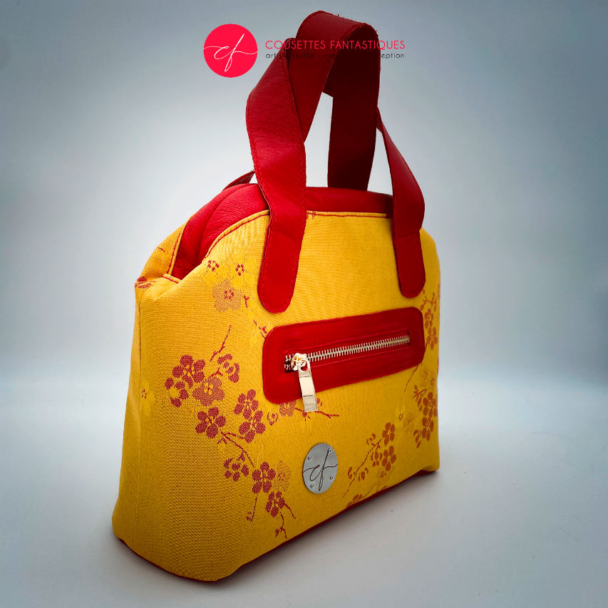 A mini handbag made of yellow upholstery fabric with a red cherry blossom pattern and red leather.