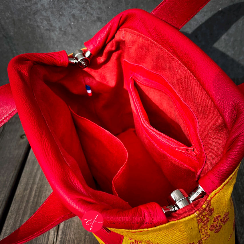 A mini handbag made of yellow upholstery fabric with a red cherry blossom pattern and red leather.